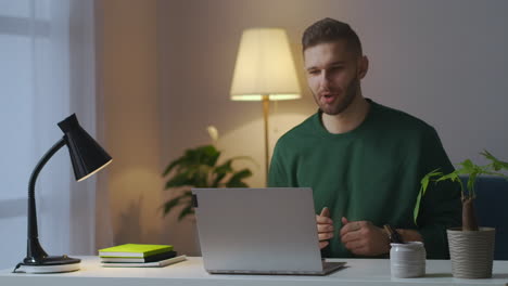 handsome-man-is-communicating-by-video-chat-by-laptop-smiling-and-gesticulating-looking-at-screen-sitting-at-home-at-evening